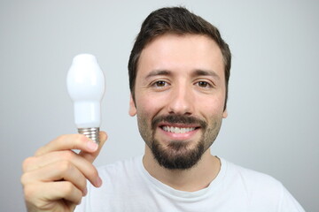 Young cheerful guy wearing white t-shirt is holding a light bulb in the hand 