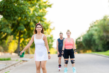 Obraz premium Group of three friends skating with inline skate in a road of a park