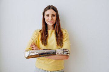 Pretty smiling blonde young woman with elegant bionic prosthesis arm looks into camera standing on...