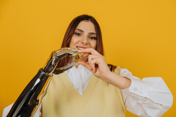 Lady with modern shiny metal bionic arm holds large golden bitcoin posing for camera on yellow...