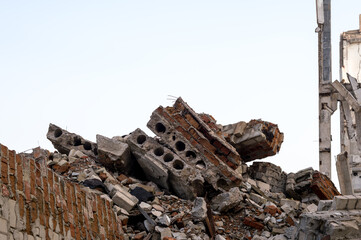 A pile of gray concrete debris, red bricks and construction debris in close-up against the remains of a destroyed building. Background