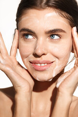 Vertical portrait of young woman washing her face with cleansing foam gel, smiling happy, cleaning...