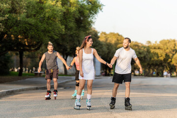 Two couples skating on inline skates holding hands on a street with trees