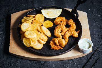 Shrimps in tempura with fried potatoes and homemade sauce on a dark background with chopsticks