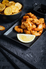 Shrimps in tempura with fried potatoes and homemade sauce on a dark background with chopsticks