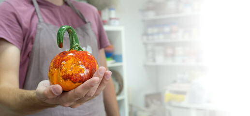 Man showing ceramic pumpkin after clay workshop lesson. Halloween eco symbol zero waste.
