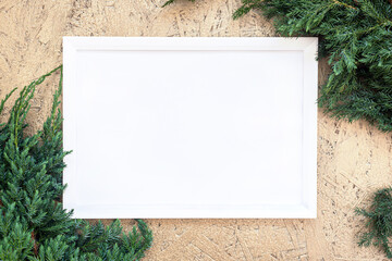 White empty frame on golden christmas background with green tree juniper branch, copy space, template for holiday greeting card.