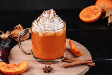 Pumpkin coffee latte with whipped cream on dark background. Hot autumn drink with cinnamon and spices in glass mug on a wooden tray.