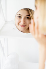 Obraz na płótnie Canvas Beauty freshness. Female dermatology. Skin health. Cheerful woman touching gorgeous radiant face at mirror reflection in light free space.