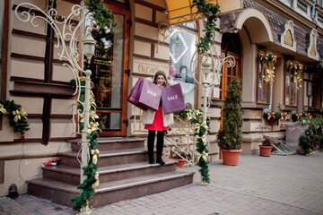 Happy girl holds paperbags with symbol of sale in the stores with sales at Christmas, around the city. Concept of shopping, holidays, happiness, Christmas Sales.