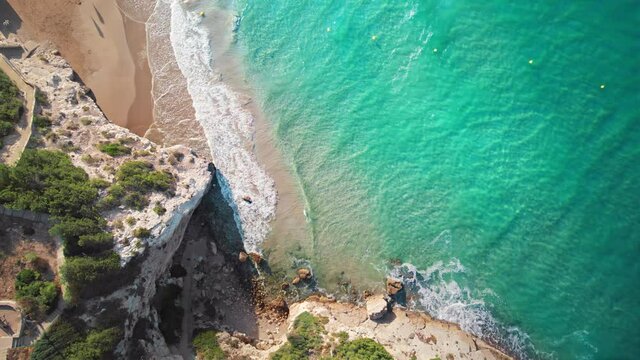 Beautiful aerial view to Mediterranean coast. Turquoise waves slowly rolling onto the sandy beach with picturesque overhanging cliffs.