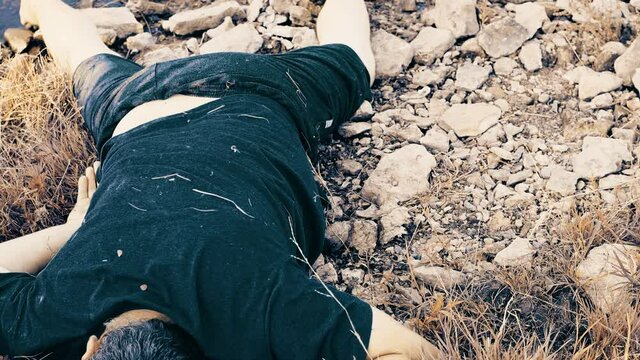 murder by the river , the body of a young man aged lies by the water, a corpse by a dirty lake unstable camera movement color correction.