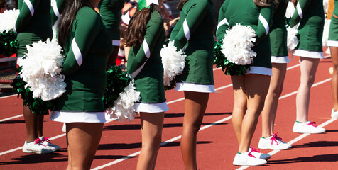 Cheerleaders in green uniforms holding white pom poms behind their backs