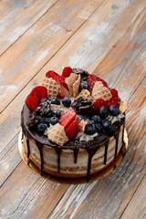 Chocolate drip cake with berries and crushed waffle cone on top, wooden table, local bakery