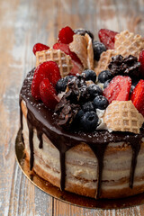 Chocolate drip cake with berries and crushed waffle cone on top, wooden table, local bakery
