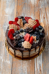 Chocolate drip cake with berries and crushed waffle cone on top, wooden table, local bakery