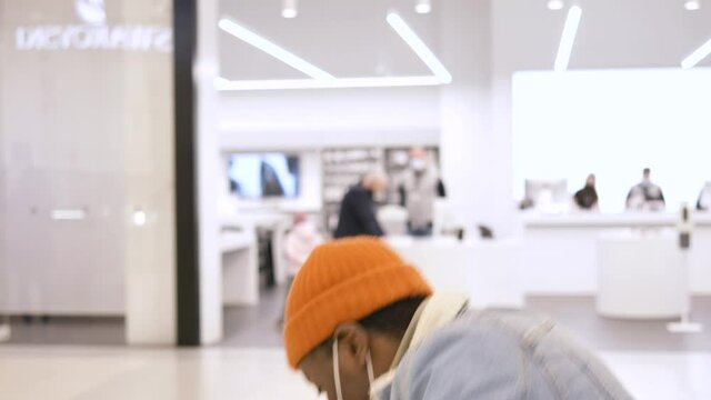 Serious shopaholic in face mask walks along shopping mall and smartphone falls from guy hands and man catches device closeup