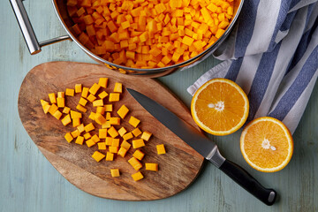 Diced pumpkin on a cutting board and in a saucepan and sliced orange