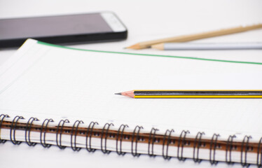 Yellow and Black graphite pen, lined notebook , smart phone on white office desk