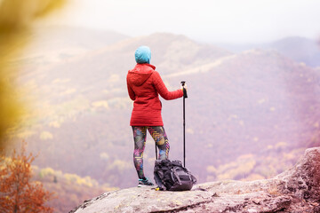 Hiking girl with poles and backpack standing on rocks. Windy autumn day. Travel and healthy...