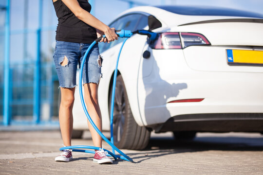 Young girl next to an electric car. Clumsy wrapped with a charging cable around her legs