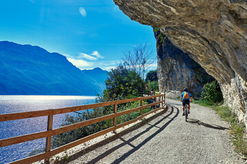 Bicyclists riding a bicycle on the  ponale street in Riva del Garda - obrazy, fototapety, plakaty