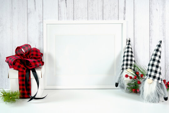 Horizontal wall art print frame product mockup. Christmas farmhouse theme SVG craft product mockup styled with gift with buffalo plaid bow and farmhouse style gnomes against a white wood background.