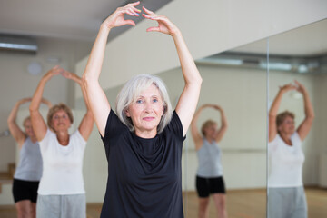 Group of three mature women performing ballet dance in exercise room.