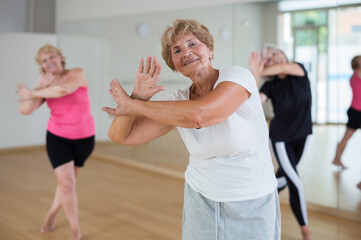 Positive senior women in sportswear dancing in fitness room.