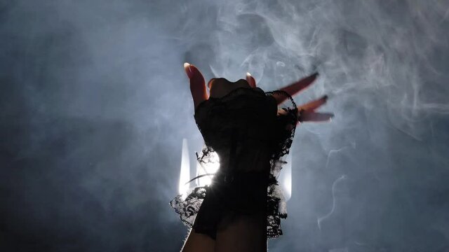 Mysterious mysterious slow dance of women's hands with ornaments in smoke against a background of bright light