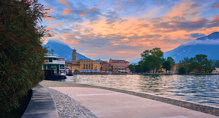 View of the beautiful Riva del Garda town at sunset with a red sky, Lake Garda surrounded by...