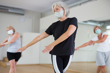 Fototapeta na wymiar Aged women in face masks performing dance during their group training in fitness room.