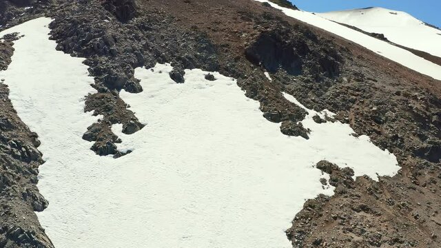 Aerial ascending drone shot up the ski slopes and mountain range in melt in spring at the Cerro Bayo ski resort near Villa La Angostura, revealing mountain peak