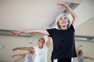 Active mature woman visiting choreography class with group of aged females, learning classical...