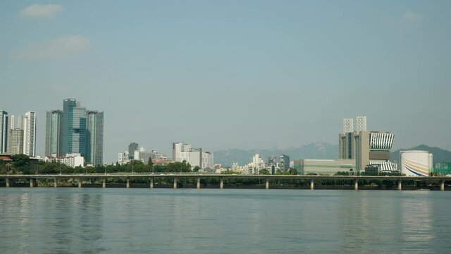 Hangang waterfront with North Seoul cityscape of Mapo-gu, Cars Traffic on Gangbyeonbuk-ro Expressway, SEAH Tower,  Mecenatpolis Shopping Mall, Bukhansan Mountains on background on sunny day, static