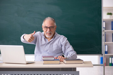 Old male teacher in front of green board