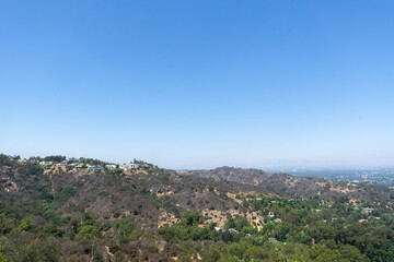 Fototapeta na wymiar View of Hollywood Hills seen from Mulholland Drive on a sunny summer day. Houses, trees and dry patches of land stretching across the valley