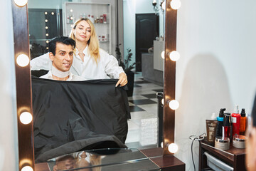 Hair stylist throwing a hairdressing cape on customer