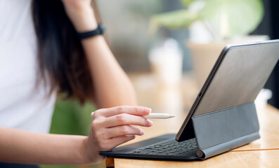 Closeup view of woman hands holding stylus pen and working on tablet computer while sitting at the...