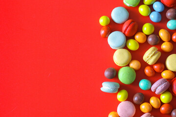 Obraz premium Top view of colorful chocolate candy and macarons on red background with copy space 