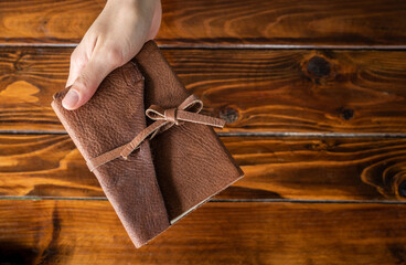 High angle view of someone hand holding a book with leather cover on wooden table. 