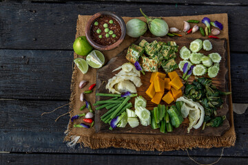 Thai Traditional Local Food : Spicy Shrimp Paste Dip or Fried shrimp paste sauce (Nam Prik Kapi) with blanched vegetables and cha-om omelets on wooden backgroud. Selective focus.