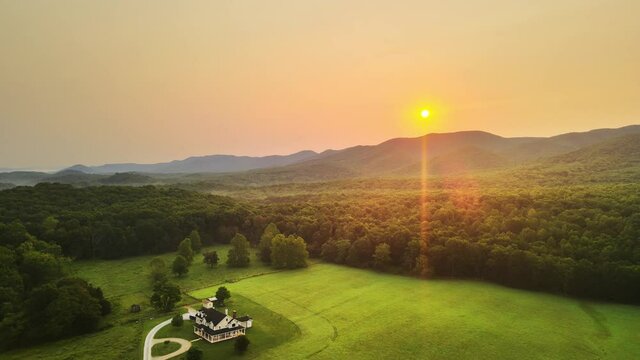 Aerial reveal shot of large upscale farm house in green field at sunrise In Forest In Country Cinematic 4K