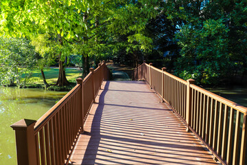 Fototapeta na wymiar a brown wooden bridge over the silky brown and green lake water surrounded by lush green and autumn colored trees at Lenox Park in Brookhaven Georgia USA