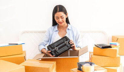 Fototapeta na wymiar Young woman freelancer working sme business online shopping and packing woman bag with cardboard box on bed at home - Business online shipping and delivery concept