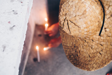 Unrecognizable person wearing woven hat lighting a candle in front of the tomb during a visit to a...