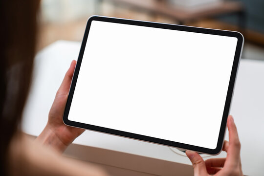 Woman hand holding digital tablet and sitting on the table in the house, mock-up of a blank screen for the application.
