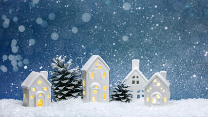 little toy christmas houses with a burning light inside and silver pine cones on blurred blue background