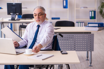 Obraz premium Old male employee in wheel-chair drinking coffee during break