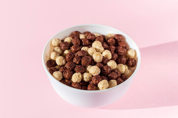 Bowl of chocolate vanilla breakfast with cereal balls on pink background. Healthy dry crispy corn balls